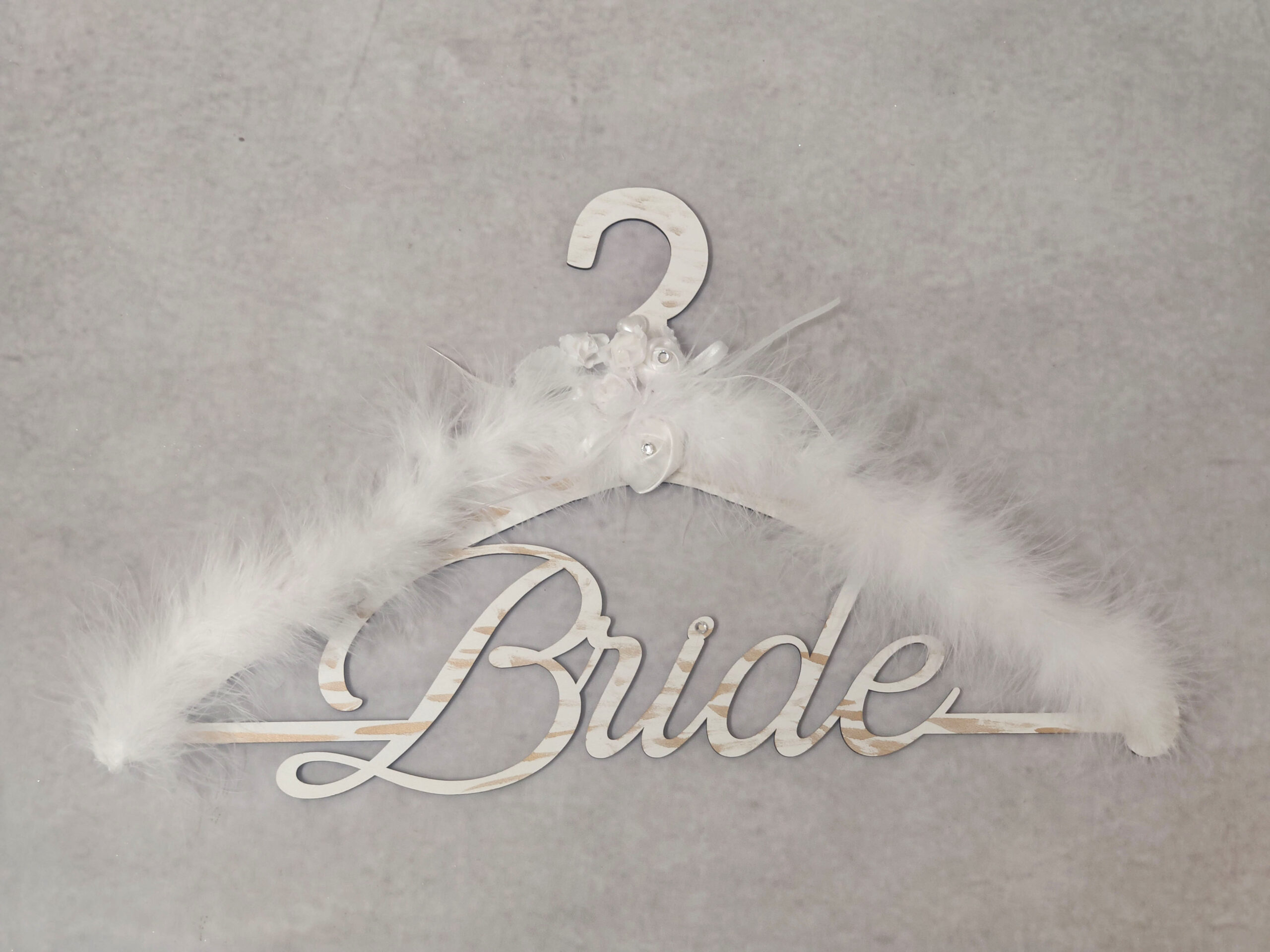 Κρεμάστρα ξύλινη με το "Bride" διακοσμημένη με πούπουλα, σατέν λευκά λουλούδια με στρας και δύο περλέ καρδιές.